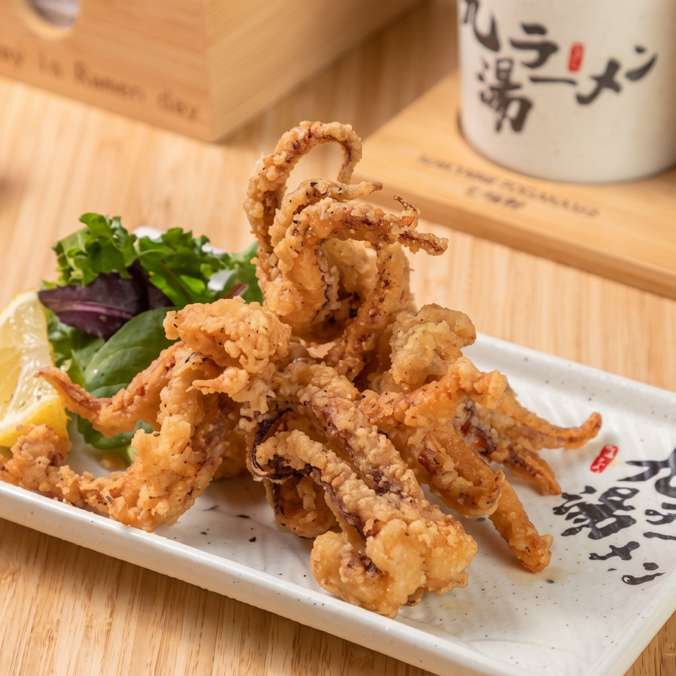Crispy fried squid tentacles arranged on a Japanese ceramic plate with lemon wedges and leafy greens.